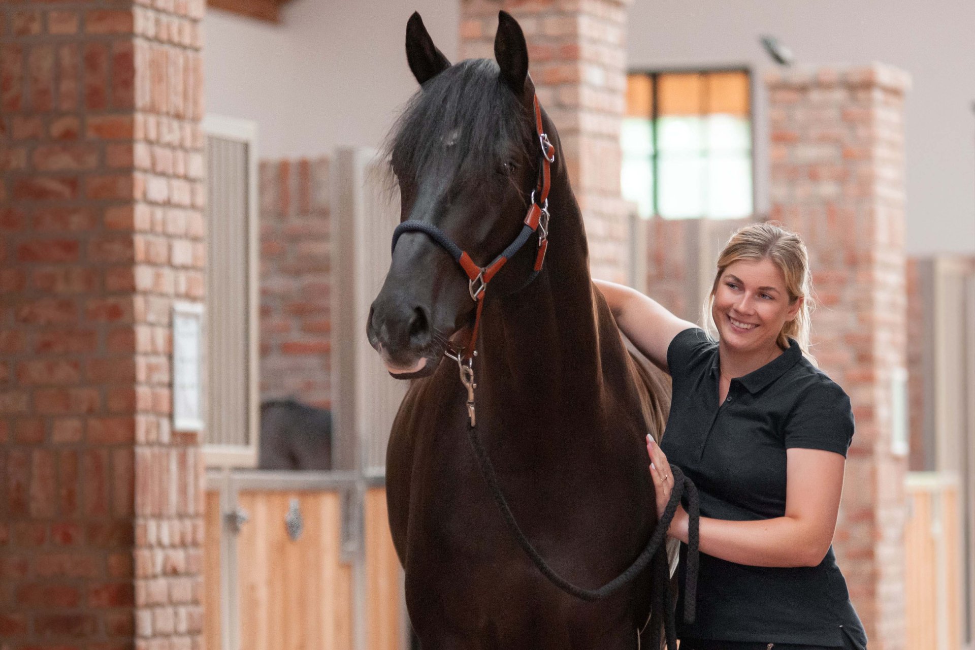 Une propriétaire d'écurie satisfaite se tient devant un box, à côté de son cheval, et lui adresse un sourire